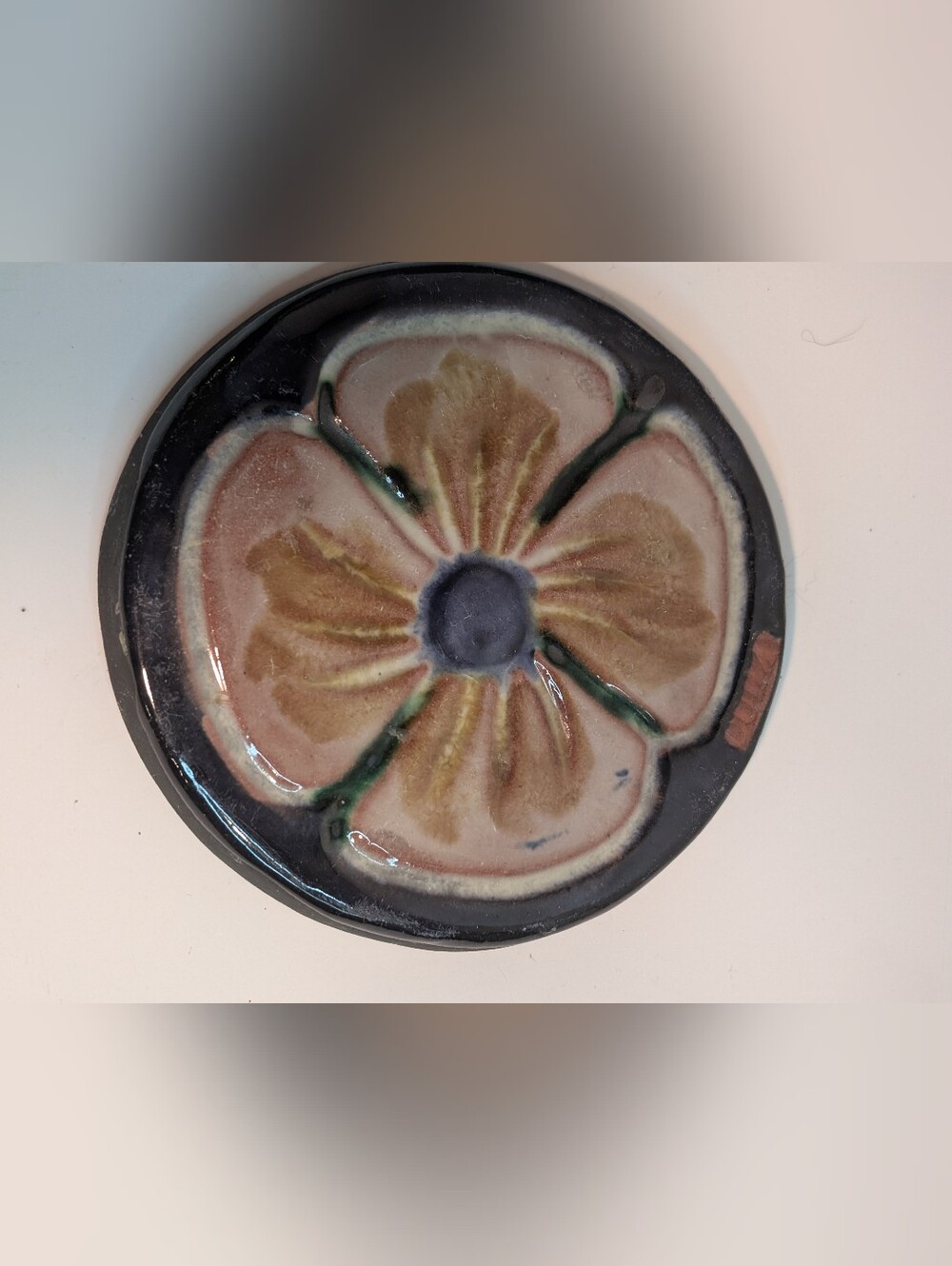 A vintage pottery tile with a floral pattern against a dark cobalt-blue.